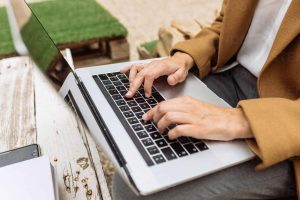 High angle of anonymous female student sitting in university courtyard with laptop and doing homework while looking at camera and smiling